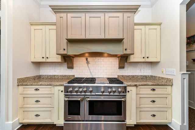 kitchen featuring backsplash, light stone counters, dark hardwood / wood-style floors, cream cabinetry, and range with two ovens