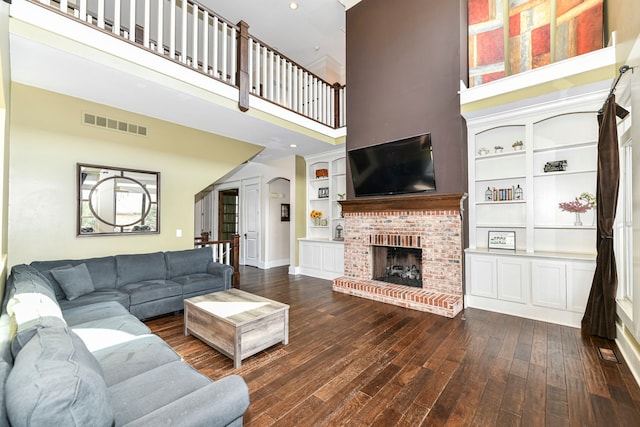 living room featuring built in features, dark hardwood / wood-style flooring, a fireplace, and a towering ceiling