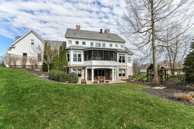 rear view of house with a playground, a lawn, a patio area, and a sunroom