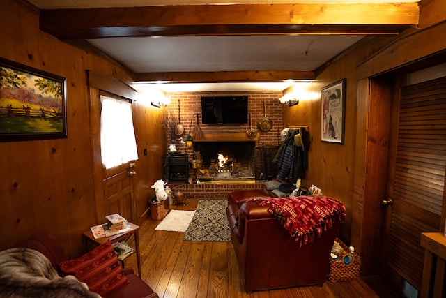 living room with dark hardwood / wood-style flooring, wood walls, beamed ceiling, and a brick fireplace