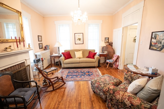 living room with a notable chandelier, a brick fireplace, hardwood / wood-style flooring, radiator, and crown molding