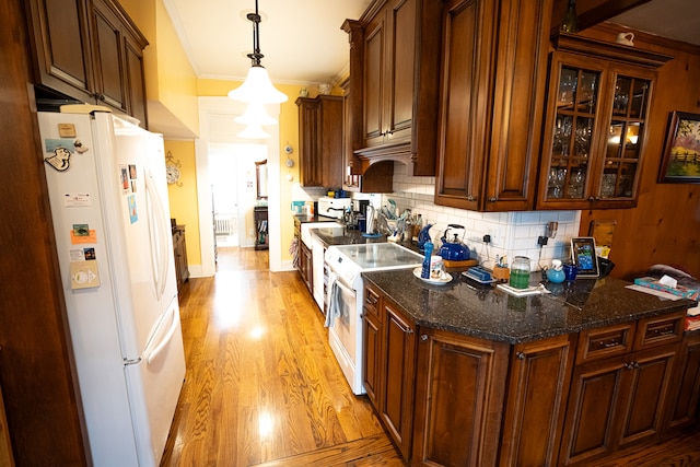 kitchen with dark stone counters, light wood-type flooring, tasteful backsplash, white appliances, and ornamental molding