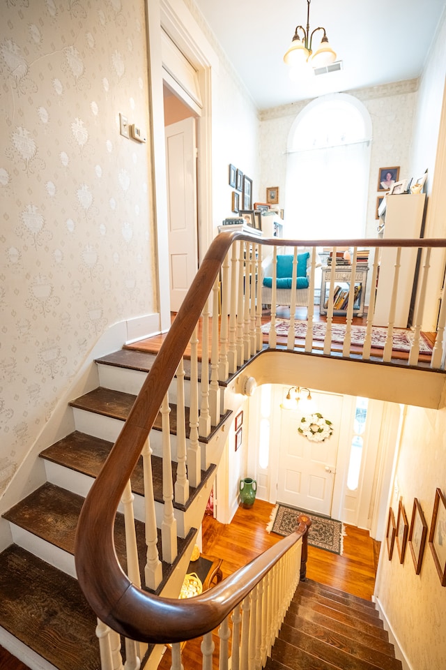 stairs with crown molding, dark wood-type flooring, and a chandelier