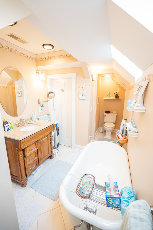 bathroom with a tub, tile flooring, oversized vanity, and toilet