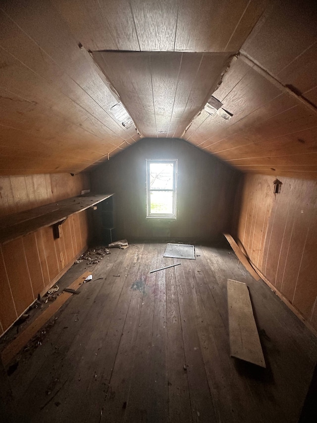 additional living space with wood walls, lofted ceiling, and dark wood-type flooring