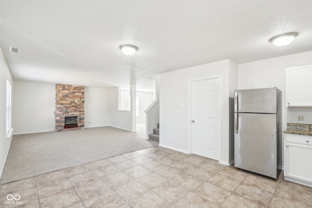 kitchen featuring white cabinetry, stainless steel refrigerator, a fireplace, dark stone counters, and light carpet