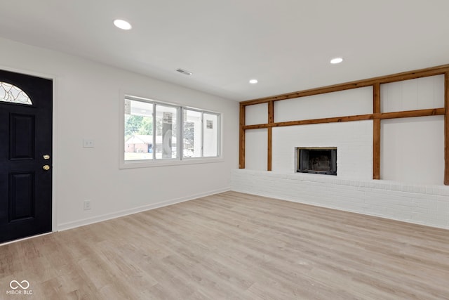 unfurnished living room featuring a brick fireplace and light wood-type flooring