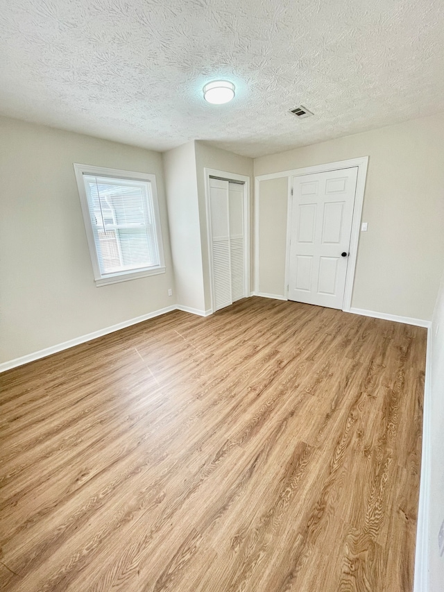 unfurnished room with a textured ceiling and light wood-type flooring