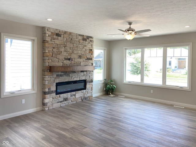 unfurnished living room with ceiling fan, wood-type flooring, a stone fireplace, and a textured ceiling