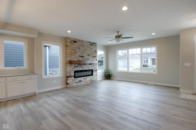 unfurnished living room with a stone fireplace, ceiling fan, and light wood-type flooring