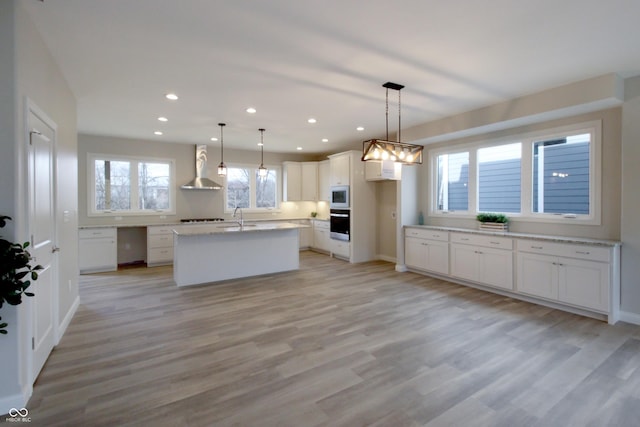 kitchen with sink, a center island, hanging light fixtures, wall chimney range hood, and white cabinets