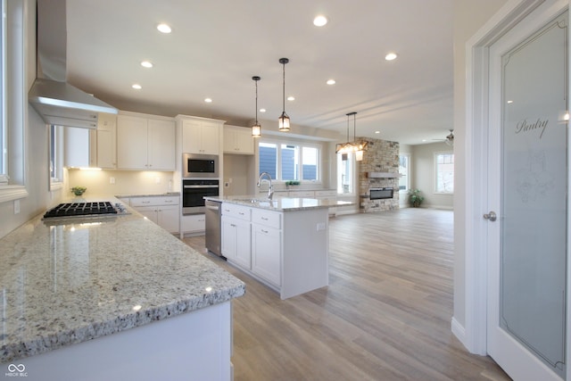 kitchen featuring pendant lighting, white cabinetry, a kitchen island with sink, stainless steel appliances, and wall chimney exhaust hood