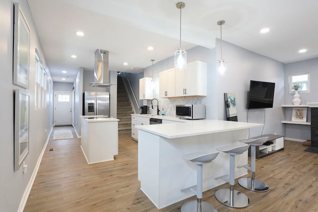 kitchen featuring appliances with stainless steel finishes, backsplash, light hardwood / wood-style floors, wall chimney exhaust hood, and white cabinets