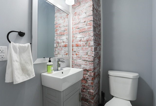 bathroom featuring brick wall, vanity, and toilet