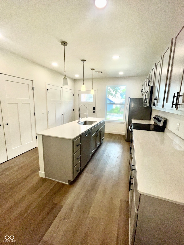 kitchen featuring stainless steel appliances, pendant lighting, hardwood / wood-style floors, a center island with sink, and sink