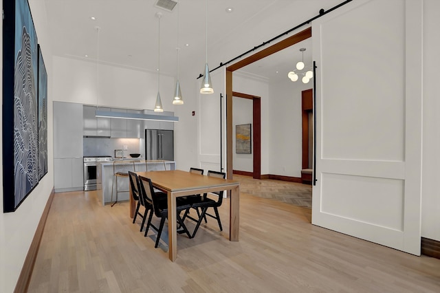 dining area with a barn door, light hardwood / wood-style flooring, and ornamental molding