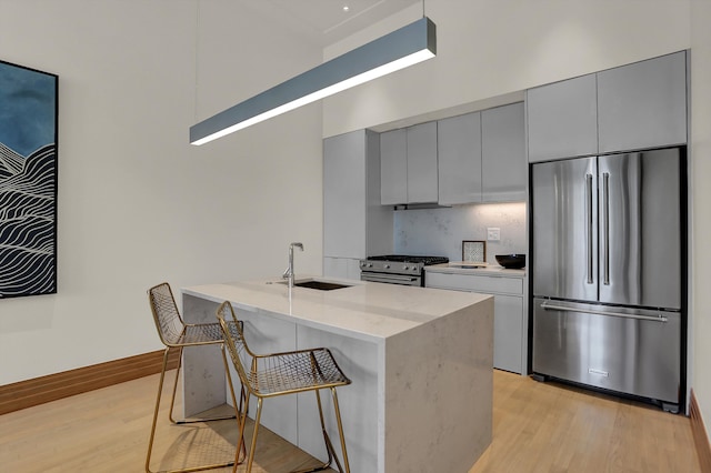 kitchen with a kitchen island with sink, sink, appliances with stainless steel finishes, and light hardwood / wood-style flooring