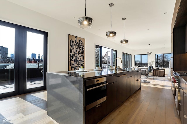 kitchen featuring sink, light hardwood / wood-style flooring, a spacious island, decorative light fixtures, and dark brown cabinets