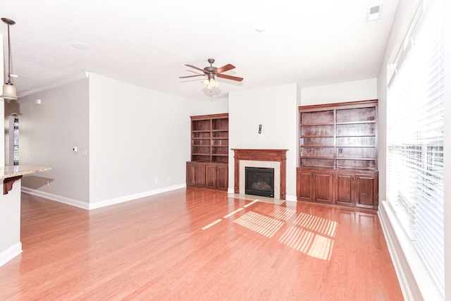 unfurnished living room with ceiling fan, light wood-type flooring, and built in shelves