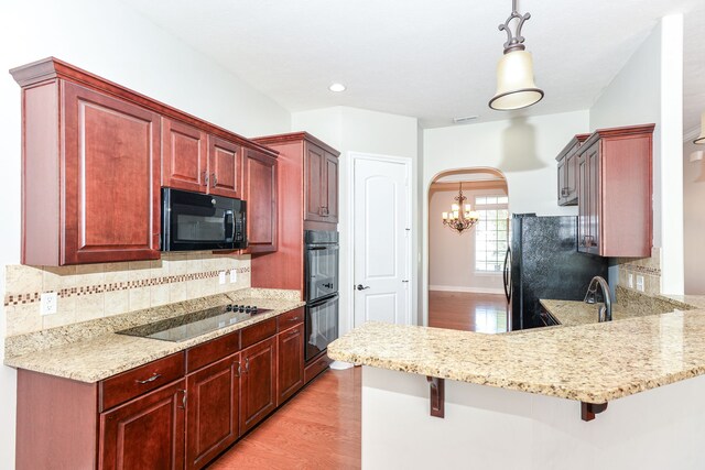 kitchen with pendant lighting, a breakfast bar, light hardwood / wood-style flooring, black appliances, and tasteful backsplash