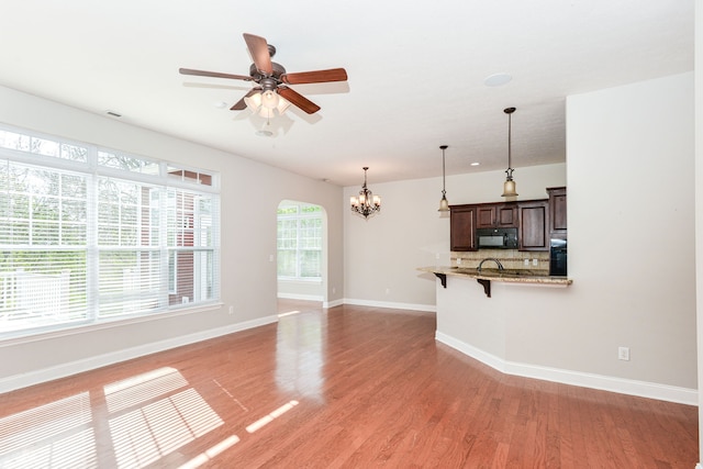 unfurnished living room featuring sink, light hardwood / wood-style flooring, and ceiling fan with notable chandelier