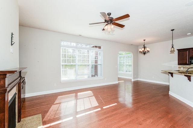 unfurnished living room featuring ceiling fan with notable chandelier and dark hardwood / wood-style floors