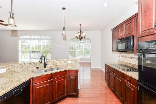 kitchen with decorative light fixtures, black appliances, sink, and light wood-type flooring