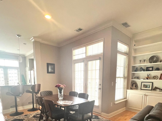 dining room featuring built in shelves, ornamental molding, and light wood-type flooring