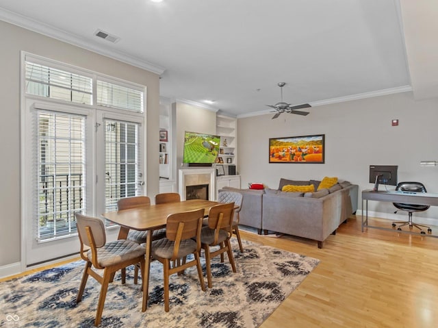 dining space with built in shelves, light hardwood / wood-style flooring, ceiling fan, and crown molding