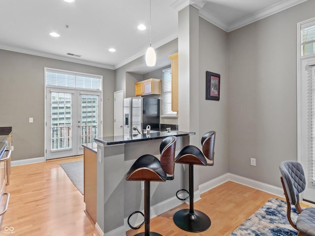 kitchen with light brown cabinets, stainless steel refrigerator with ice dispenser, hanging light fixtures, a kitchen bar, and kitchen peninsula