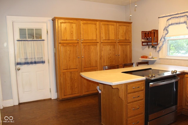 kitchen with a kitchen bar, kitchen peninsula, stainless steel electric range oven, and dark wood-type flooring