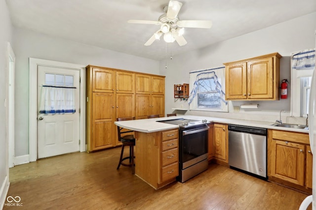 kitchen with ceiling fan, sink, stainless steel appliances, kitchen peninsula, and a kitchen bar