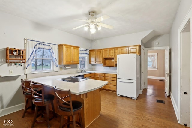 kitchen featuring black electric stovetop, white refrigerator, ceiling fan, a kitchen bar, and kitchen peninsula