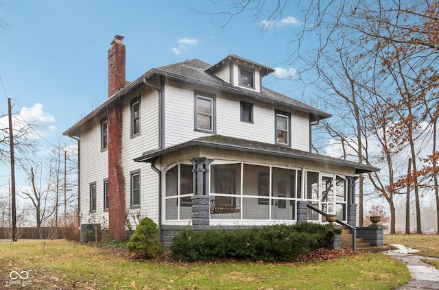 american foursquare style home with a front yard, roof with shingles, a sunroom, and a chimney