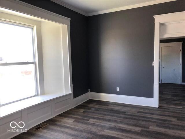 empty room featuring dark wood-type flooring and ornamental molding