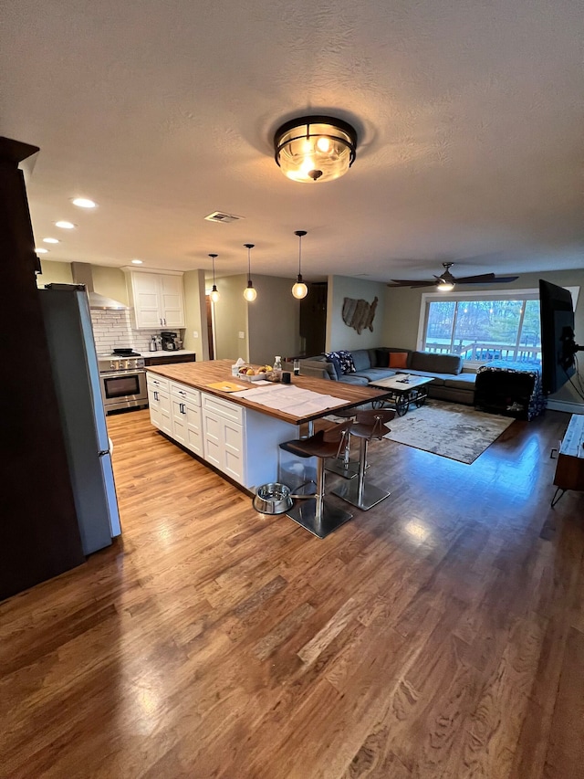 kitchen with black refrigerator, ceiling fan, light hardwood / wood-style floors, white cabinets, and wall chimney range hood