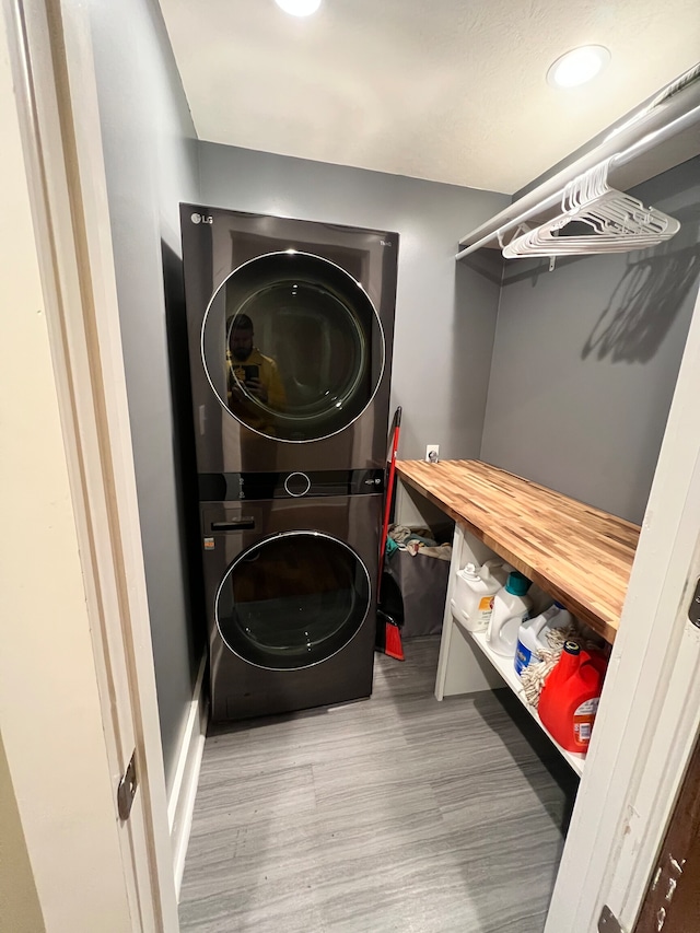 clothes washing area with stacked washing maching and dryer and light wood-type flooring