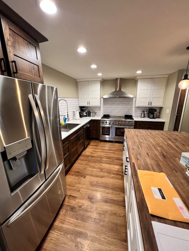 kitchen featuring hanging light fixtures, light hardwood / wood-style flooring, stainless steel appliances, white cabinets, and wall chimney exhaust hood