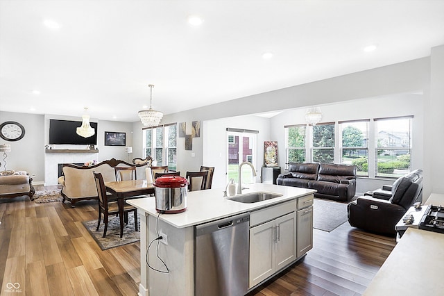 kitchen with decorative light fixtures, dishwasher, wood-type flooring, sink, and an island with sink