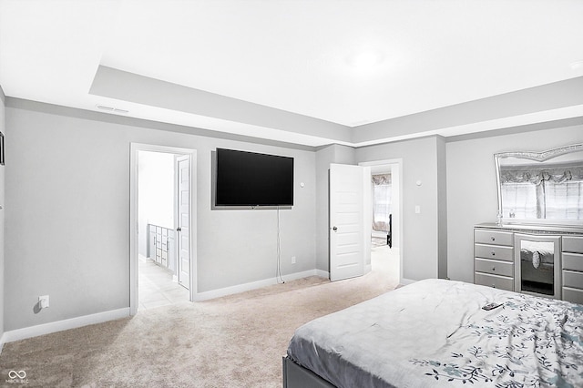 carpeted bedroom featuring ensuite bath and a raised ceiling