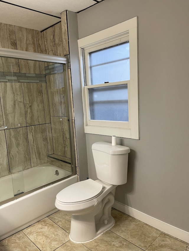 bathroom with tile flooring, toilet, and combined bath / shower with glass door