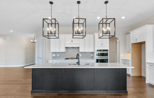 kitchen with hanging light fixtures, an island with sink, sink, and white cabinetry