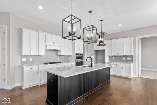 kitchen with sink, a kitchen island with sink, hanging light fixtures, stainless steel appliances, and white cabinets