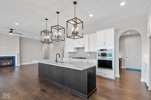 kitchen with sink, hanging light fixtures, appliances with stainless steel finishes, a kitchen island with sink, and white cabinets