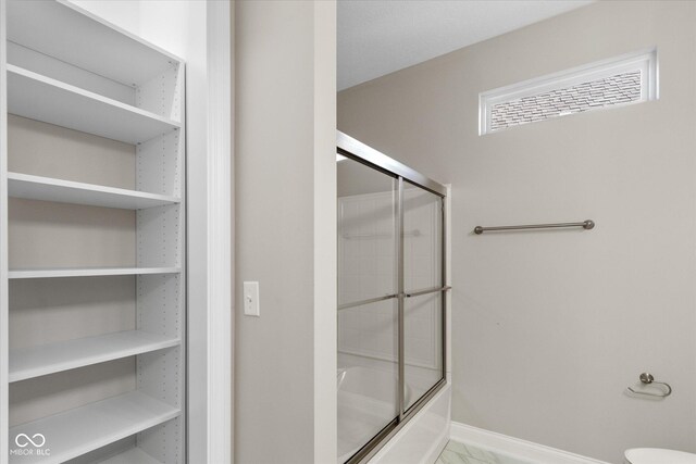 bathroom with bath / shower combo with glass door and toilet