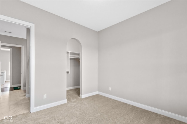 unfurnished bedroom featuring a walk in closet, a closet, and light carpet