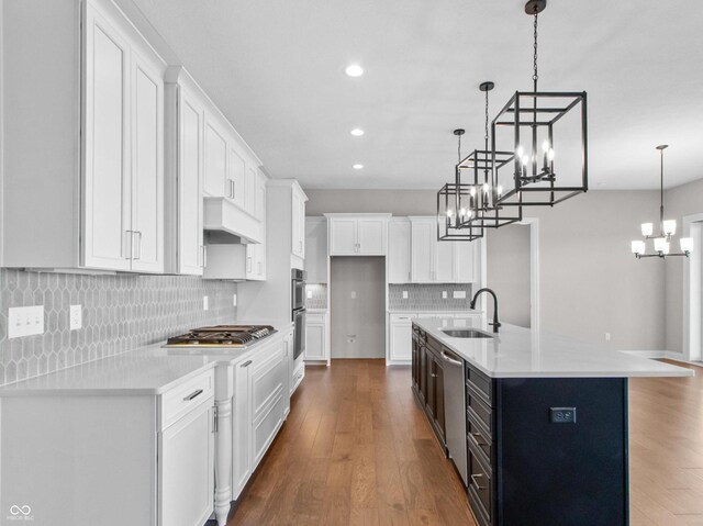 kitchen featuring sink, white cabinetry, hanging light fixtures, stainless steel appliances, and an island with sink