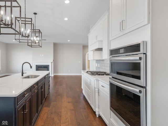 kitchen with pendant lighting, sink, appliances with stainless steel finishes, white cabinetry, and an island with sink