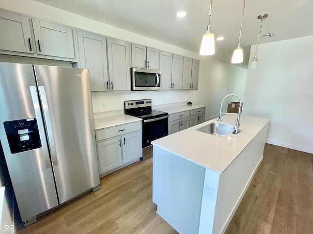 kitchen with stainless steel appliances, pendant lighting, an island with sink, sink, and light hardwood / wood-style floors