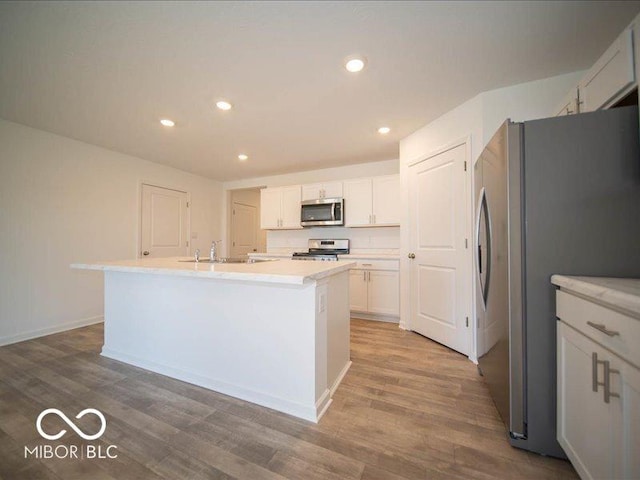 kitchen with a center island with sink, white cabinets, sink, wood-type flooring, and stainless steel appliances